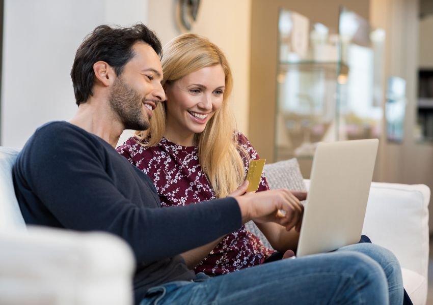 Two property owners look at online lease templates on a silver laptop as they sit on a couch beside each other.